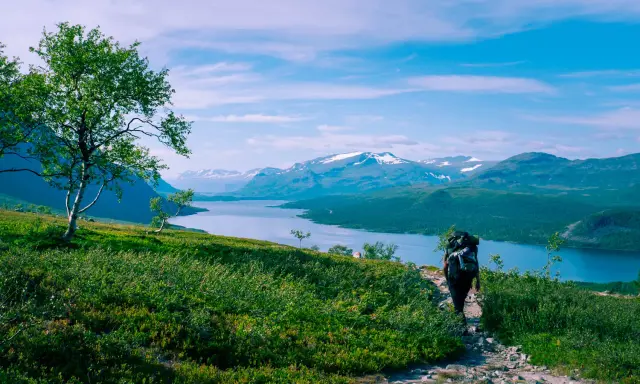 Vandra i Norrland med storslagen utsikt över sjö och snöklädda berg. En ensam vandrare med ryggsäck går på en stenstig.