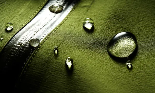 Gocce d'acqua su tessuto verde, dimostrando il significato di "water repellent".