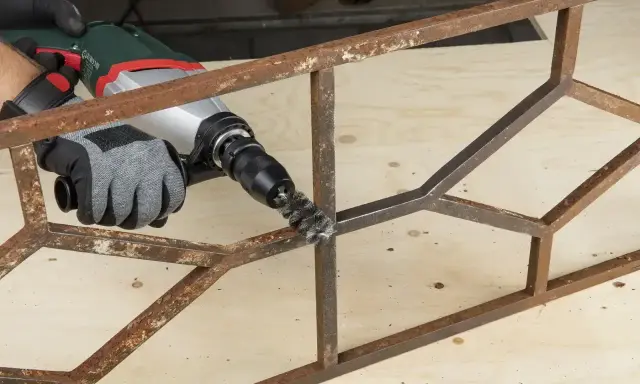 Rękawica z metalową szczotką na wiertarce usuwa rdzę z metalowej konstrukcji. Skuteczny sposób, jak odrdzewić metal.