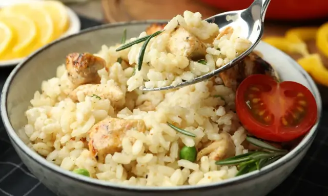 Kremowe risotto z kurczakiem, groszkiem i rozmarynem, udekorowane pomidorkiem. Idealne na obiad.