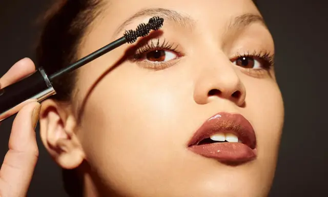 Una mano aplica máscara de pestañas a unos ojos pequeños, resaltando su belleza natural.