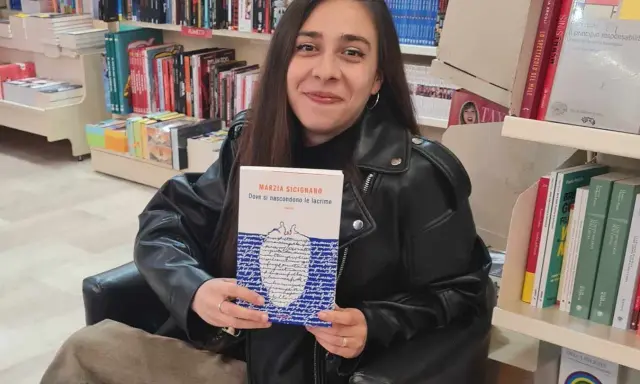 Una giovane donna sorride in libreria, tenendo in mano il libro "Dove si nascondono le lacrime".