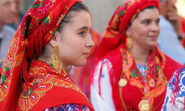 Giovani donne con foulard rossi ricamati e grandi orecchini dorati, un'immagine che evoca la tradizione di fare il portoghese con eleganza.
