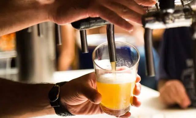 Ręka nalewa złociste piwo do szklanki. Czy alkoholik może pić piwo bezalkoholowe? To pytanie, na które odpowiedź zależy od indywidualnej sytuacji.