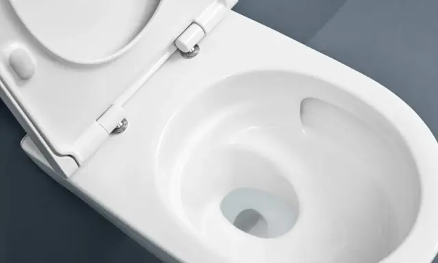 Vue rapprochée d'une cuvette de WC blanche, siège relevé, suggérant le sens d'ouverture de la porte des toilettes.
