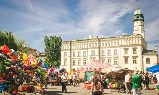 Kolorowy jarmark na rynku na Kazimierzu w Krakowie. Balony, stragany z pamiątkami i ludzie spacerujący pod jasnym niebem.