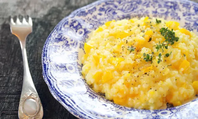 Pyszny, kremowy ryż do risotto z kawałkami dyni, posypany świeżym tymiankiem i pieprzem. Obok leży elegancki widelec.