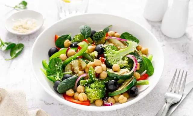 Ensalada de legumbres vibrante con garbanzos, brócoli, espinacas, aceitunas negras y pimientos verdes.