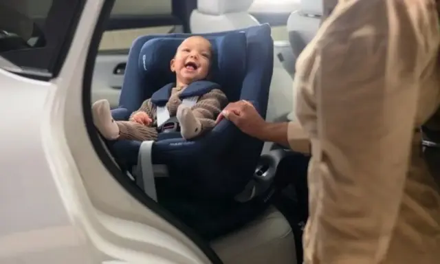 Bebé sonriente en un maxicosi azul, listo para aprender como colocar el maxicosi en el coche.