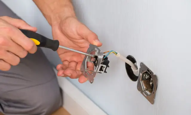 Instalacja gniazdka z uziemieniem. Ręce przykręcają mechanizm do puszki, podłączając przewody.