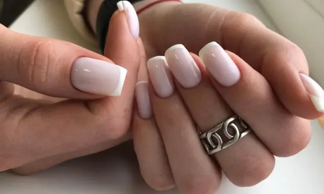 Dłonie z idealnym french manicure. Paznokcie prostokątne w delikatnym różu z białymi końcówkami, ozdobione srebrnym pierścionkiem.