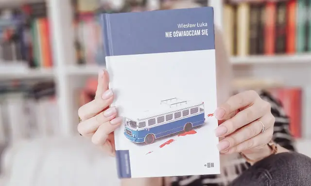 Dłonie trzymają książkę "Nie oświadczam się" z okładką przedstawiającą niebieski autobus i plamy krwi.