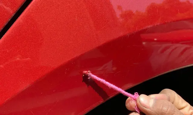 Różowa nitka z farbą na czerwonym lakierze auta, próba zrobienia zaprawki.