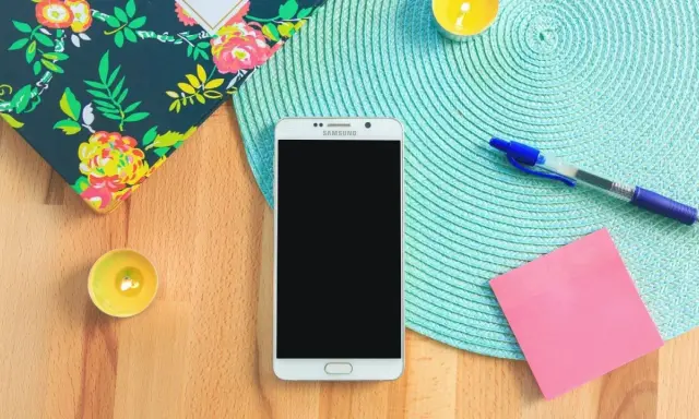 Un smartphone prêt à vous aider à vous organiser au quotidien. Un carnet fleuri, des bougies, un stylo et un post-it rose complètent la scène.