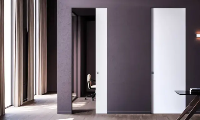 Paredes blancas y puertas de color blanco y morado oscuro, con una silla de oficina y un escritorio.