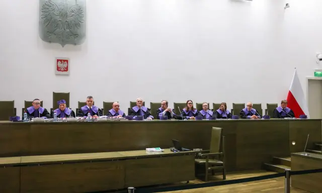 Sędziowie w togach siedzą za stołem w sali sądowej, przygotowując się do rozprawy przed trybunałem stanu.