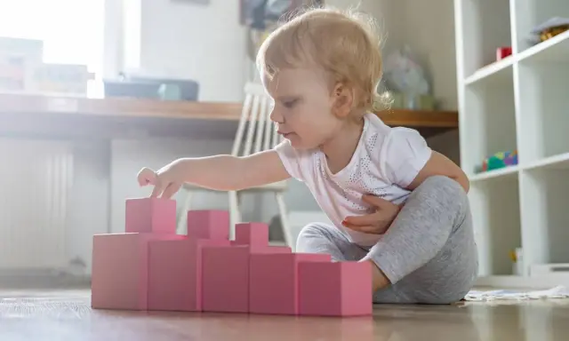Bambina bionda gioca con blocchi rosa, ideali come giochi montessori 6 mesi fai da te per sviluppare la coordinazione.