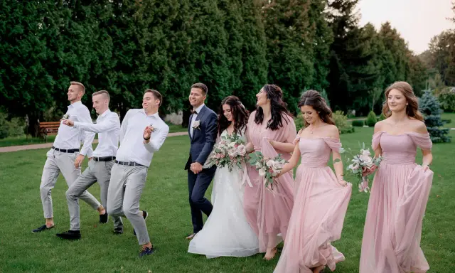 Para ślubna z drużbami i druhnami w eleganckim ubiorze na ślub, idący przez trawnik.