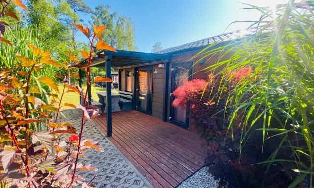 Uroczy tiny house wynajem. Drewniany domek z tarasem, otoczony zielenią i kwitnącymi krzewami. Idealne miejsce na relaks.