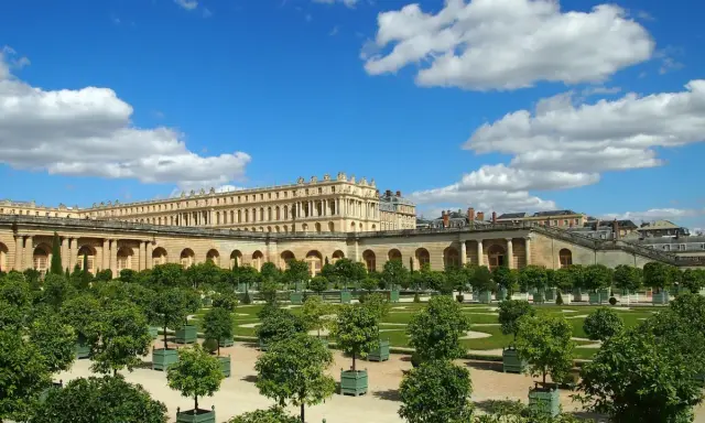 Jardines del Palacio de Versalles, un lugar lleno de curiosidades, con árboles en macetas y un cielo azul con nubes.