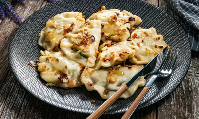 Pyszne pierogi, jak przygotować mrożone pierogi, podane na talerzu z zasmażoną cebulką.