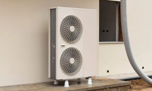 Une pompe à chaleur monobloc, avec ses deux ventilateurs, est installée à l'extérieur d'un bâtiment en construction.