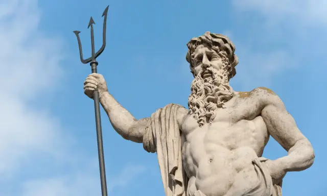 Statue de Poseidon dieu des mers, tenant son trident, sous un ciel bleu.