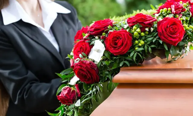 Kalie na pogrzeb, wieniec z czerwonych róż i zieleni, spoczywa na drewnianej trumnie.