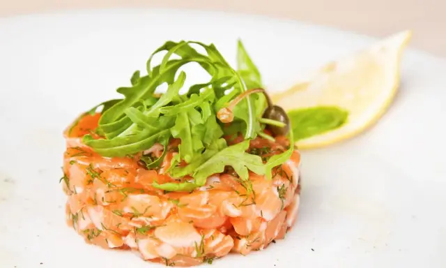 Un délicieux tartare de saumon frais, garni de roquette et d'une tranche de citron, prêt à être dégusté.