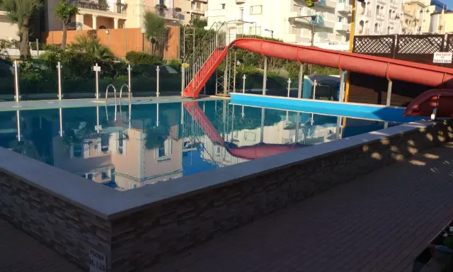 Piscina con scivolo rosso e giochi d'acqua ai Bagni Carmen Cattolica. Riflessi degli edifici nell'acqua azzurra.