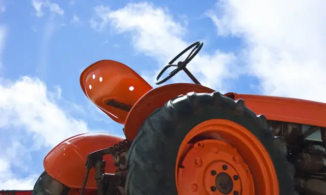 Close-up of an orange tractor's wheel and seat against a blue sky with clouds. This vintage tractor, possibly a different size Kubota tractor, awaits its next task.