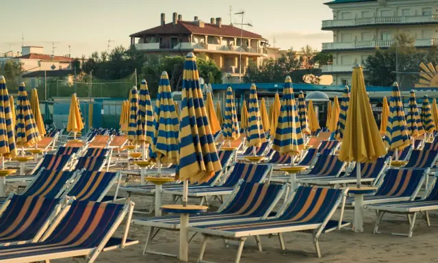 File di sdraio e ombrelloni a righe blu e gialle sulla spiaggia di Cervia Milano Marittima, pronti per accogliere i bagnanti.