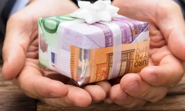 Dłonie trzymają prezent opakowany w banknoty euro. To pomysł, jak zapakować pieniądze na prezent dla dziecka, tworząc unikalną niespodziankę.
