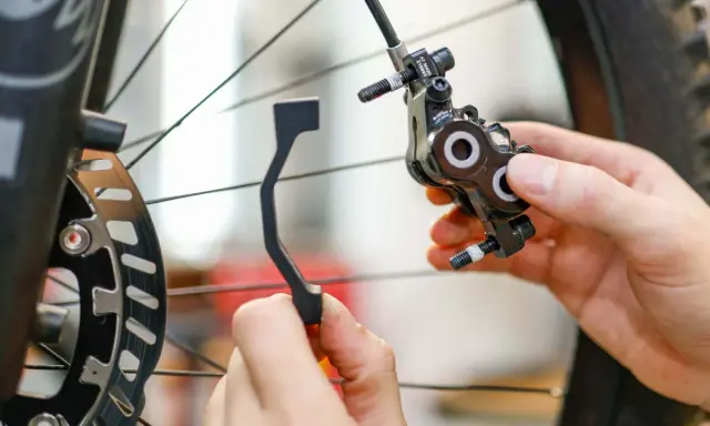 Hände montieren eine Fahrrad-Scheibenbremse. Ein Adapter wird gehalten, um ein Schleifen der Scheibenbremse zu verhindern.