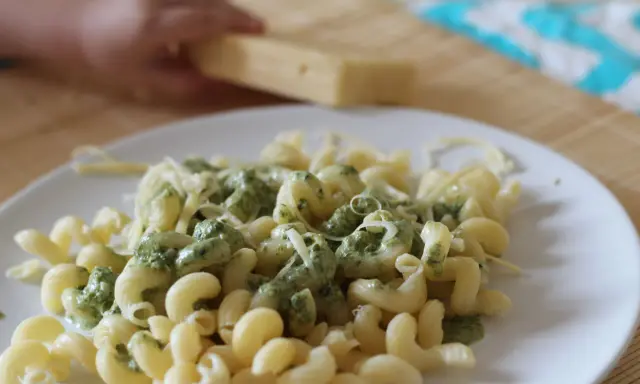 Pyszny makaron ze szpinakiem i parmezanem, gotowy do podania. Dziecko pomaga w przygotowaniu.