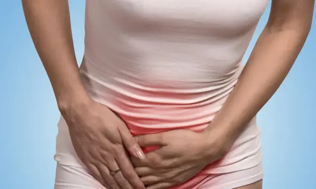 Kobieta trzyma się za brzuch, odczuwając ból w pachwinie. Czerwone zaczerwienienie sugeruje stan zapalny.