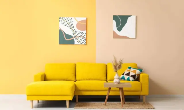 Un divano giallo acceso in una stanza con pareti bicolore. I colori della stanza sono vivaci e moderni, con due quadri astratti che completano l'arredamento.