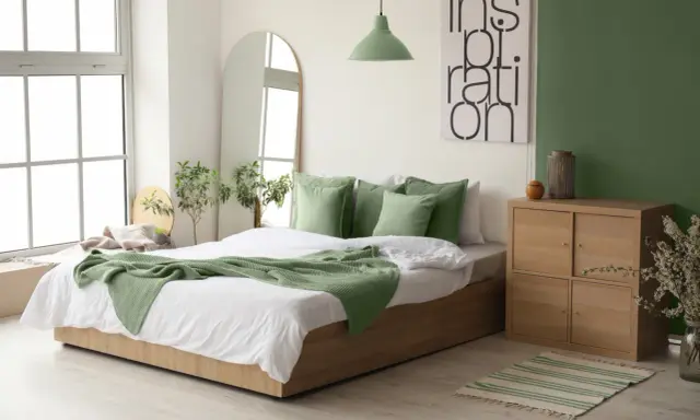 Chambre au nord lumineuse avec murs blancs et un mur vert sauge. Le lit est orné de coussins et d'une couverture vert menthe, apportant une touche de fraîcheur.