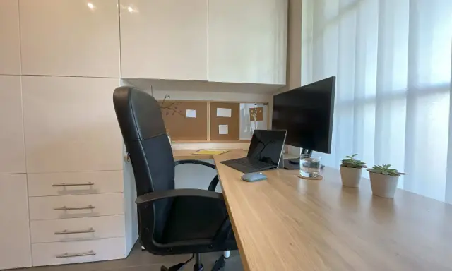 Un coin bureau moderne et fonctionnel pour aménager votre espace de travail. Chaise noire, bureau en bois, écran, ordinateur portable et plantes vertes.