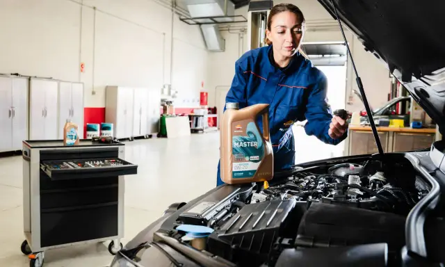 Mecánica muestra cómo cambiar el aceite del coche, sosteniendo una botella de aceite Repsol Master.