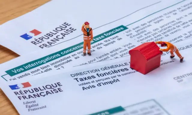 Figurines sur des documents fiscaux français. L'une pousse une maison rouge, symbolisant la taxe foncière pour un revenu modeste.