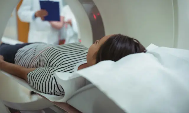 Pacjentka leży na łóżku rezonansu magnetycznego, obok niej stoi lekarz z dokumentacją.