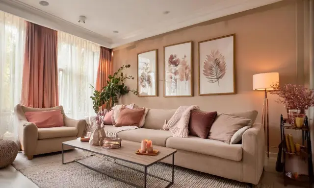 Un salon coloré et chaleureux, avec un canapé beige, des coussins roses et des tableaux de feuilles.