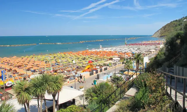 Spiaggia affollata a Gabicce Mare, con file infinite di ombrelloni colorati e lettini. Le recensioni la descrivono come un paradiso estivo.