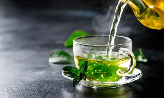Un thé fumant à la menthe poivrée est versé dans une tasse transparente, ornée d'une feuille de menthe fraîche.