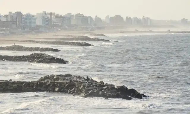 Olas rompen contra una escollera de rocas, protegiendo una ciudad costera. El escollera significado es claro: barrera contra el mar.