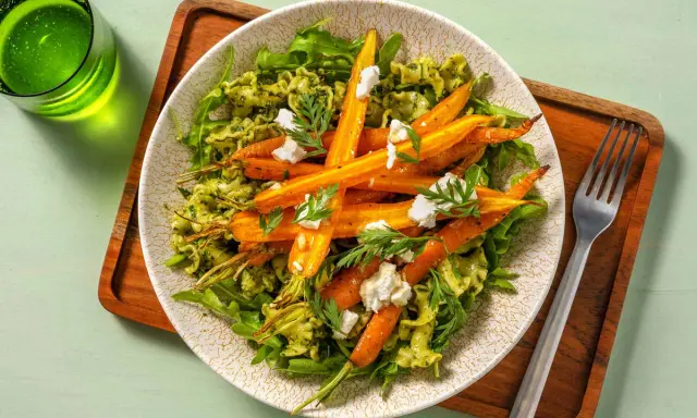 Pâtes vertes avec des carottes rôties et du fromage émietté, garnies de fanes de carottes fraîches.