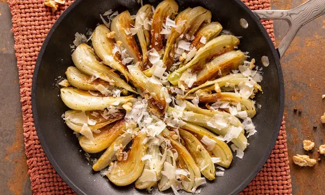 Finoçchi gratinati in padella, dorati e saporiti, guarniti con scaglie di formaggio e noci croccanti.