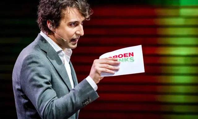 Man met krullend haar, in grijs pak, houdt een papier met "GROENLINKS" vast. Discussie over de Moslimbroederschap?