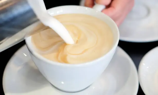 Milch wird in eine Tasse mit Kaffee gegossen, um ein cremiges Café au Lait zu kreieren.